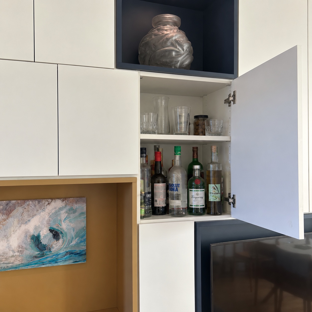 Porte ouverte sur un rangement intérieur avec étagère, verres et bouteilles